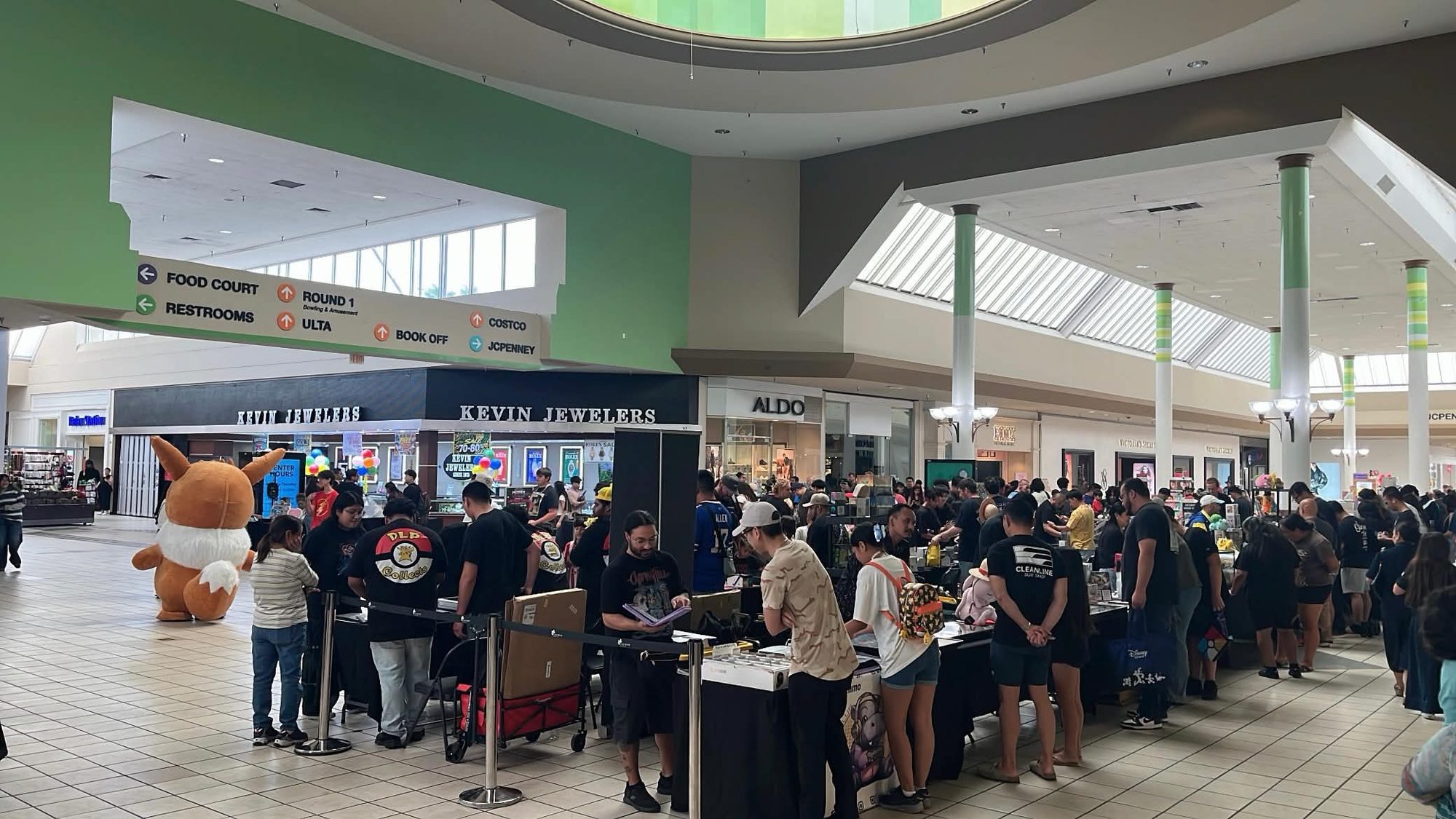 Busy vendor aisle with an Eevee mascot near Kevin Jewelers